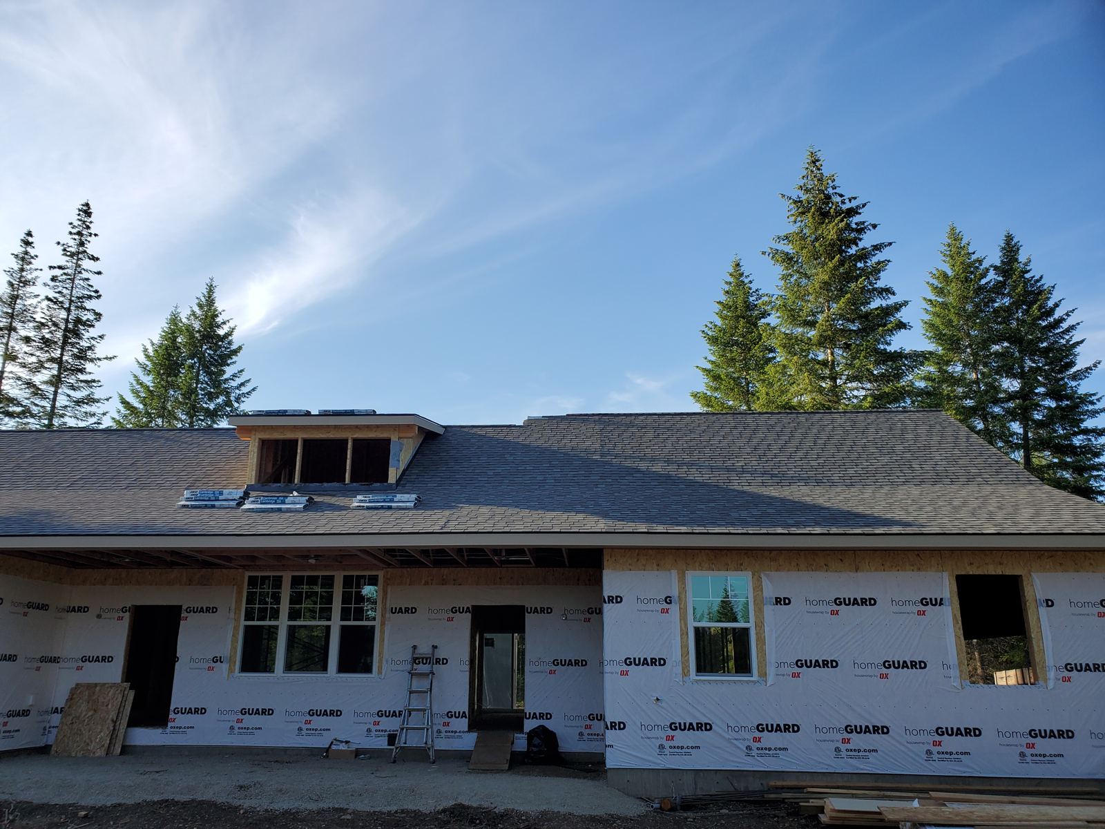 House under construction with roof shingles and housewrap on exterior walls, framing stage